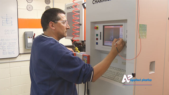 Toolmaker in safety glasses programming a wire EDM machine at its control panel