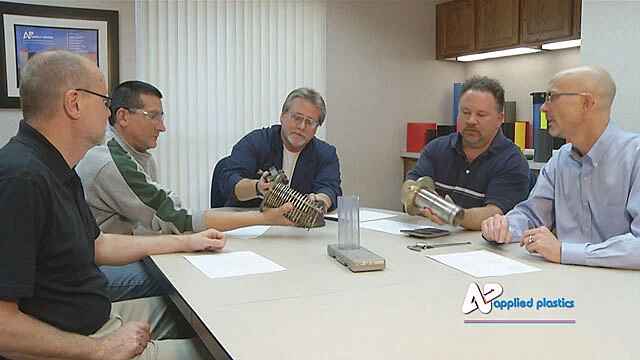 Applied Plastics staff reviewing extrusion tooling and sample parts around a conference table