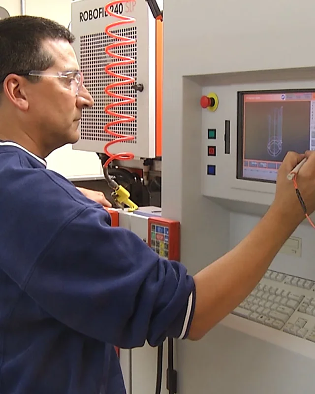 Worker in safety glasses operating a wire EDM machine touchscreen