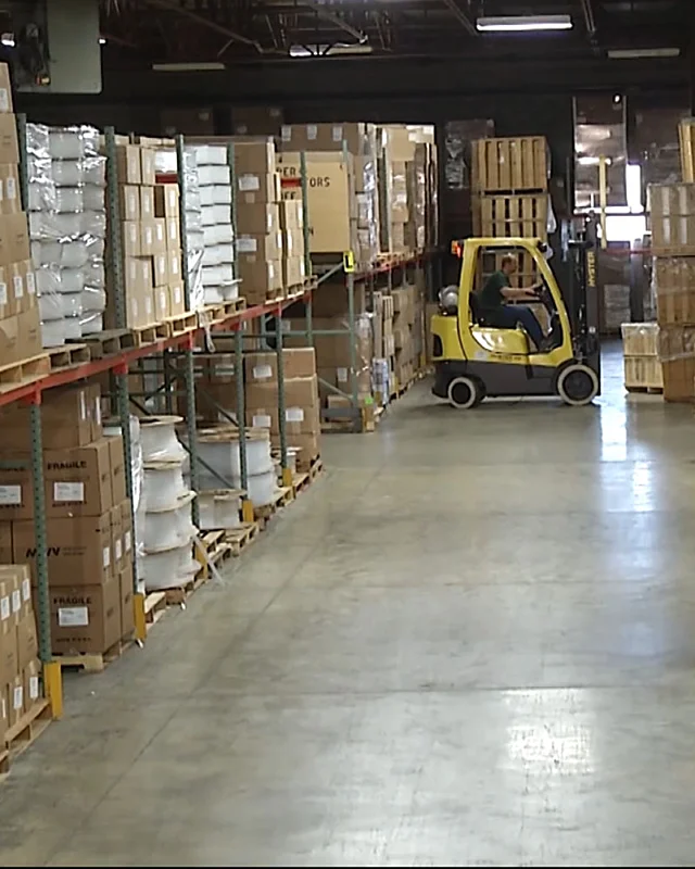 Forklift driver in a warehouse aisle lined with racked pallets and cartons