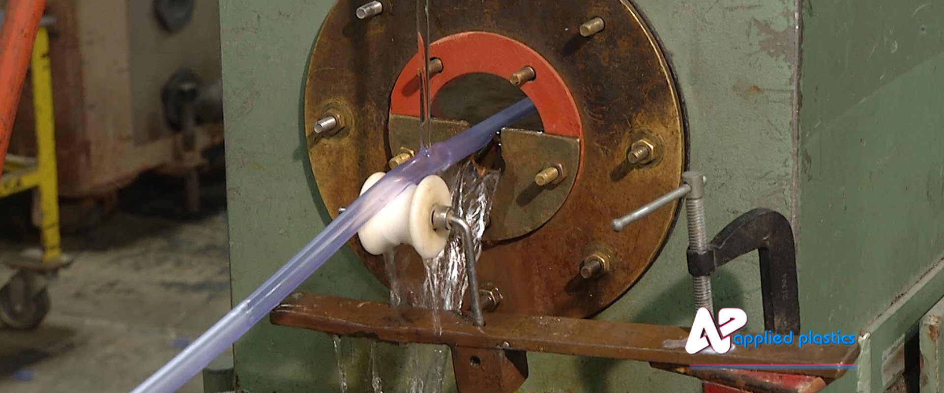 Clear plastic tubing leaving an extrusion die and running over a guide roller under cooling water